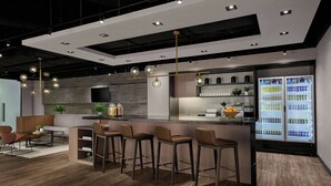 A modern bar area with a long counter, multiple stools, and a refrigerator stocked with beverages.