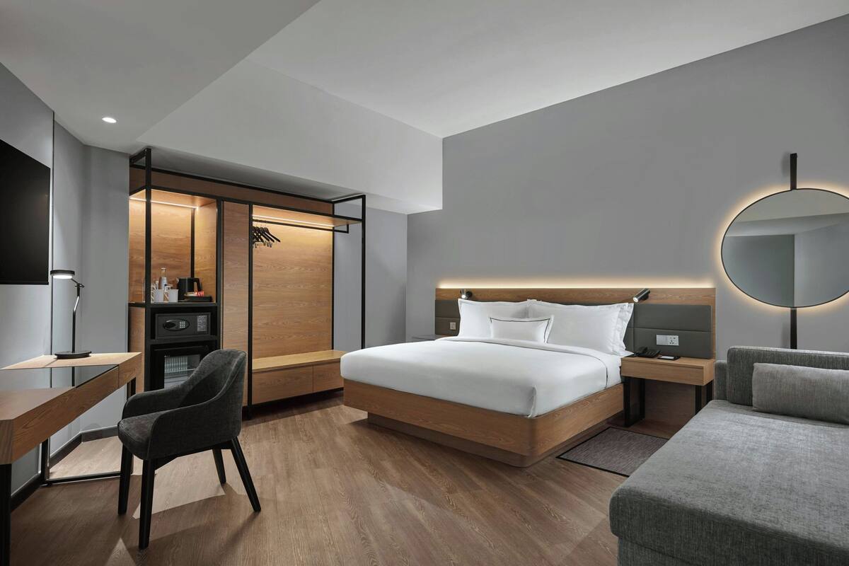 Ein modernes Hotelzimmer mit Bett, Nachttisch, Sessel, Schreibtisch und Kleiderschrank.