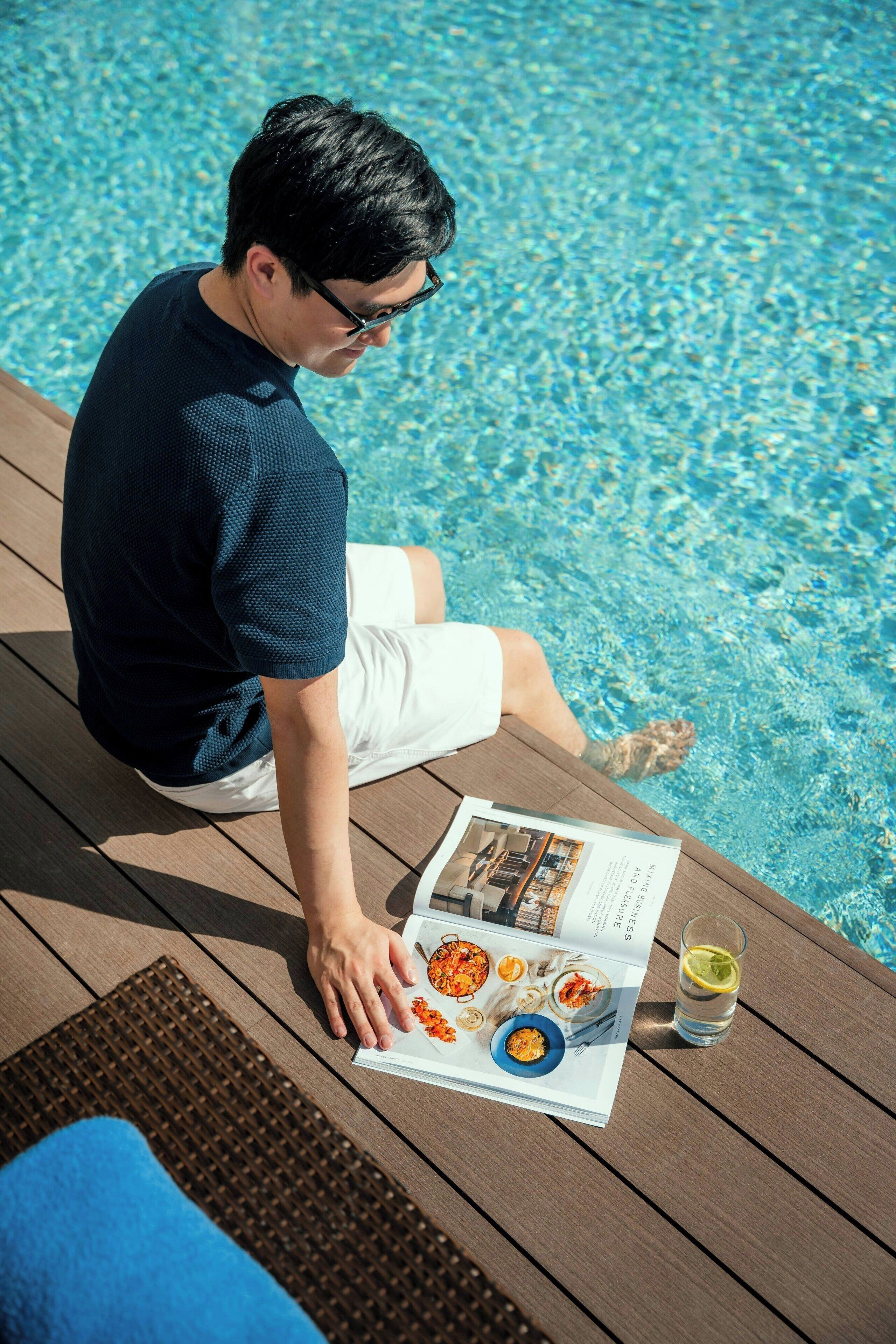 A person sitting by a poolside with a menu and a glass of water.