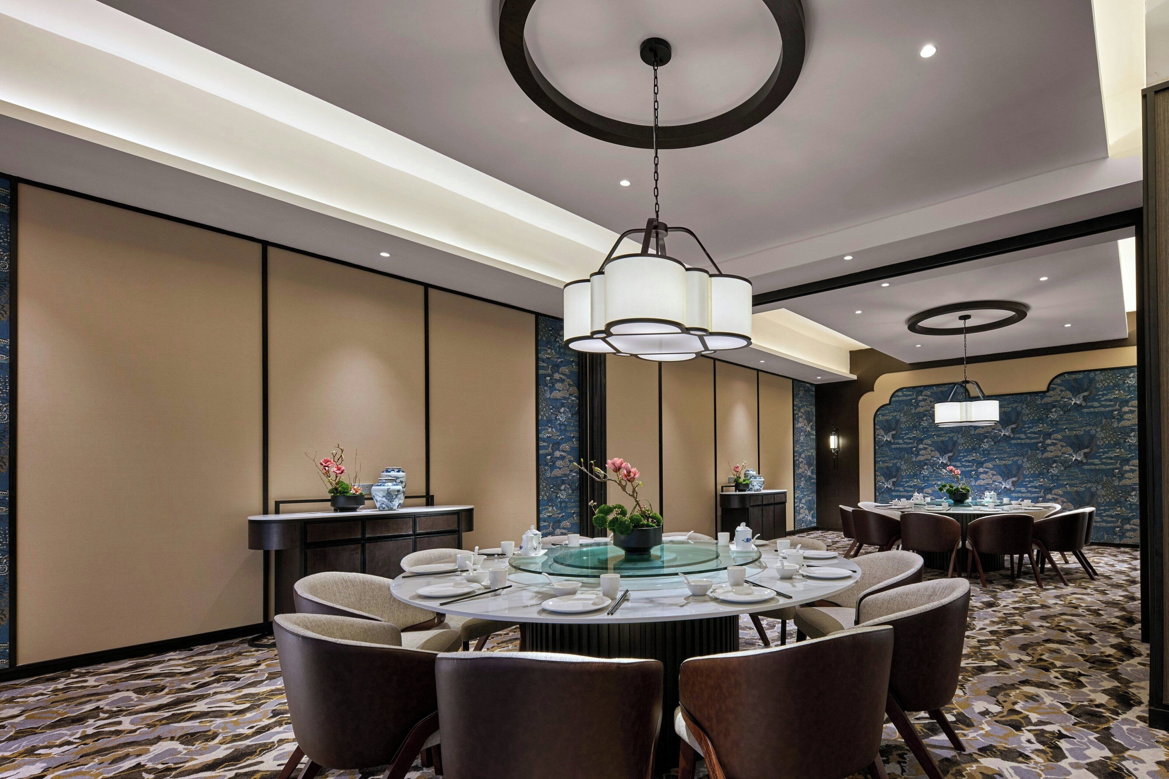 A hotel dining area with round tables, chairs, and a central chandelier.