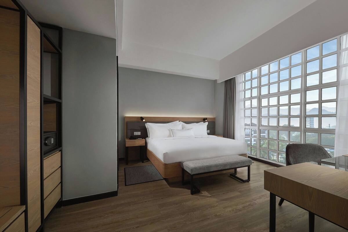 Ein modernes Hotelzimmer mit einem großen Bett, einem Schreibtisch und Blick auf die Stadt durch große Fenster.