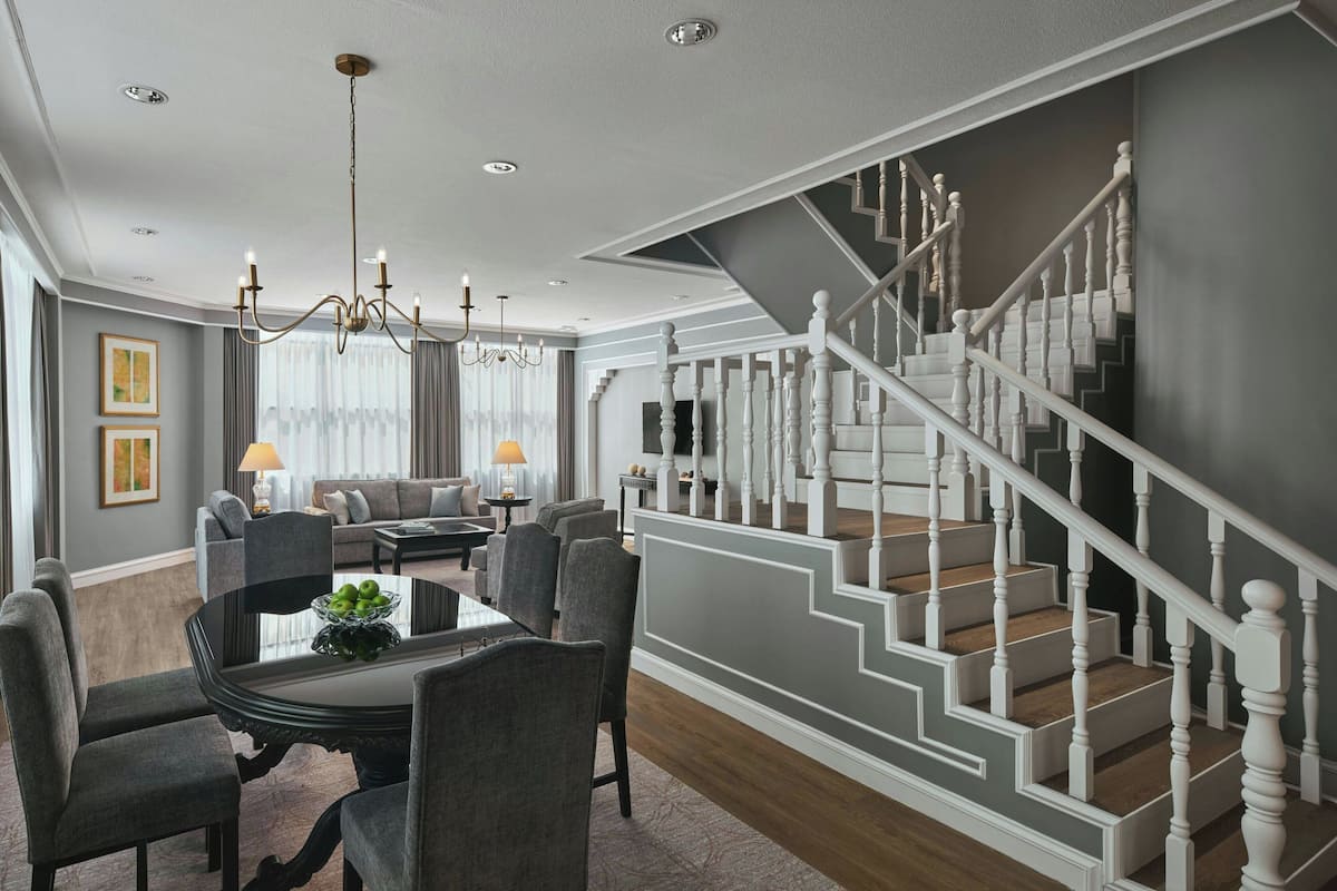 Ein modernes Wohnzimmer mit Essbereich, einer Treppe und einem Chandelier.