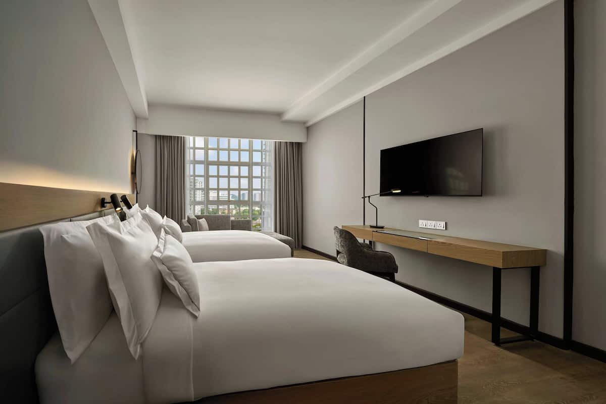 Ein modernes Hotelzimmer mit zwei Betten, einem Fernseher, einem Schreibtisch und Blick auf die Stadt.