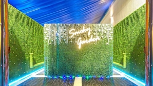 A room with a green foliage wall, a neon sign reading "Snaky Garden," and a brick floor. - Zain International Hotel (Dubai)