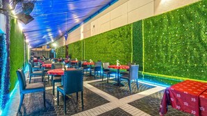 An indoor dining area with tables and chairs, a green wall, and a blue ceiling. - Zain International Hotel (Dubai)