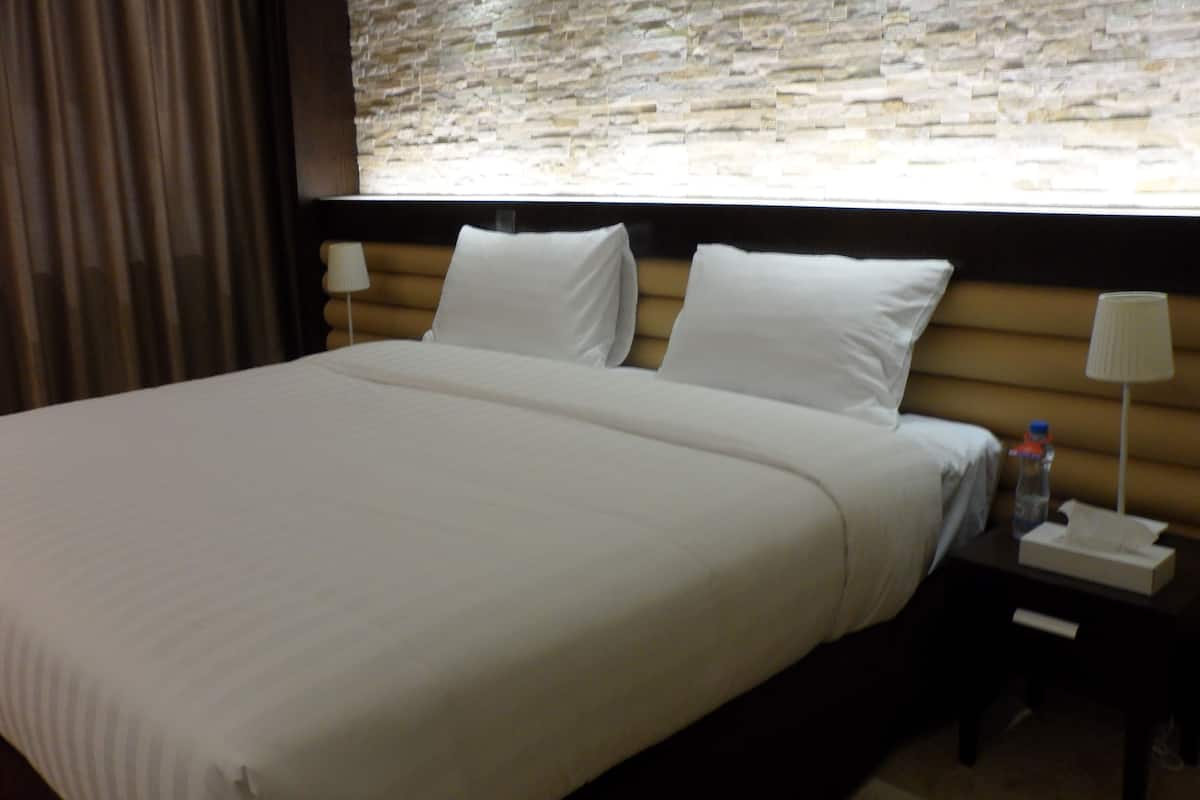 Habitación de hotel con una cama grande, una mesita de noche con lámpara, una botella de agua y una caja de pañuelos.