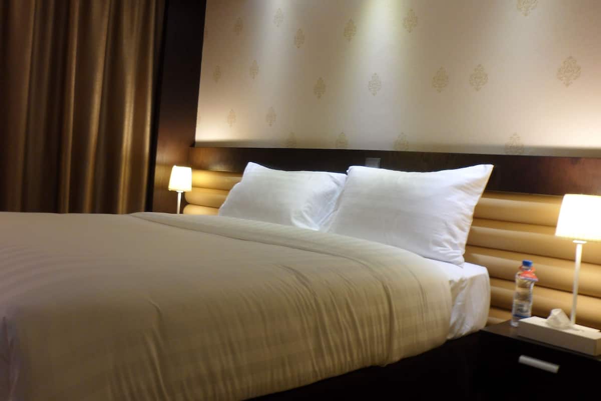 Una habitación de hotel con una cama grande, dos lámparas de noche, una botella de agua y una mesita de noche.