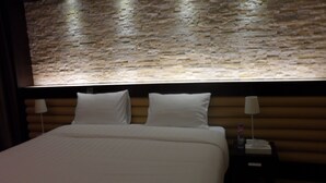 A hotel room with a large bed, two pillows, a wooden headboard, and a stone wall. - Mark Inn Hotel Deira (Dubai)