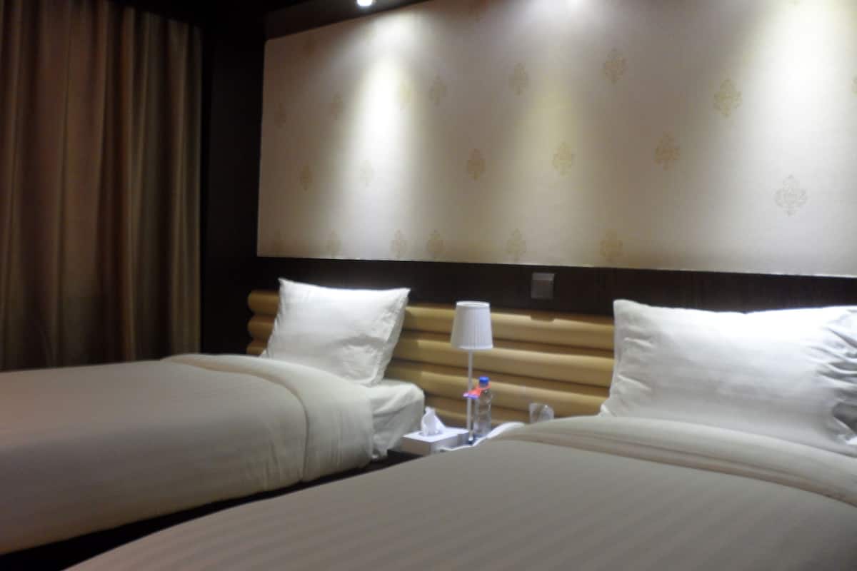 Habitación de hotel con dos camas, cabeceros, una lámpara y una botella de agua en la mesita de noche.