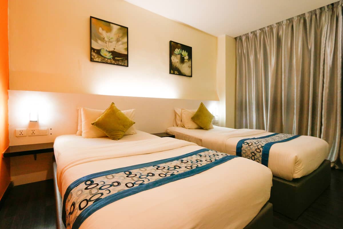 A hotel room with two beds, each with a pillow and a patterned bedspread. There are two wall-mounted paintings above the beds.