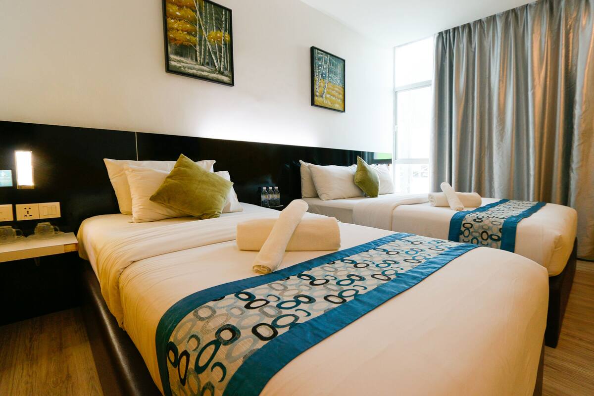 A hotel room with two beds, a headboard, a nightstand, and artwork on the wall.