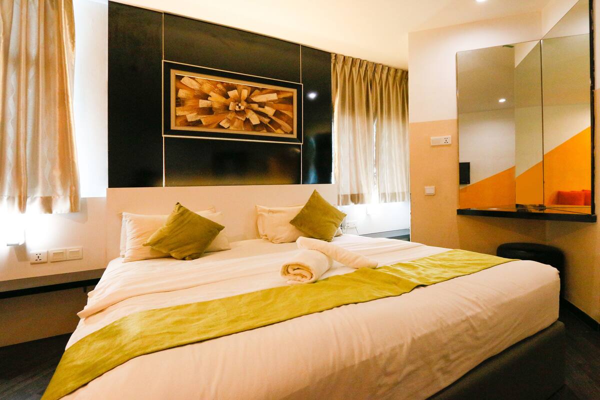 A neatly made bed with white linens and green accents, a large mirror, and a modern wall art piece.