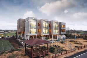 A modern multi-story hotel with large windows, a covered outdoor seating area, and a well-maintained lawn.