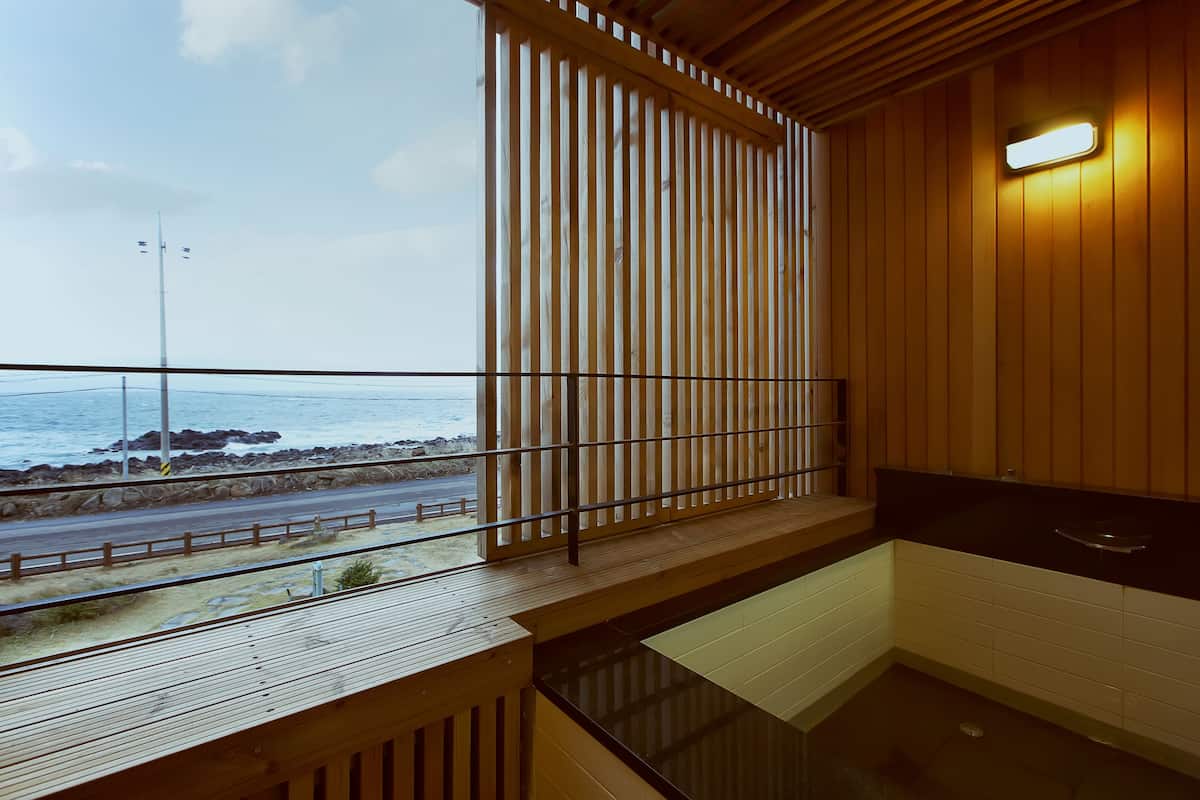 A wooden interior with a view of the sea, a wooden deck, and a bathtub.