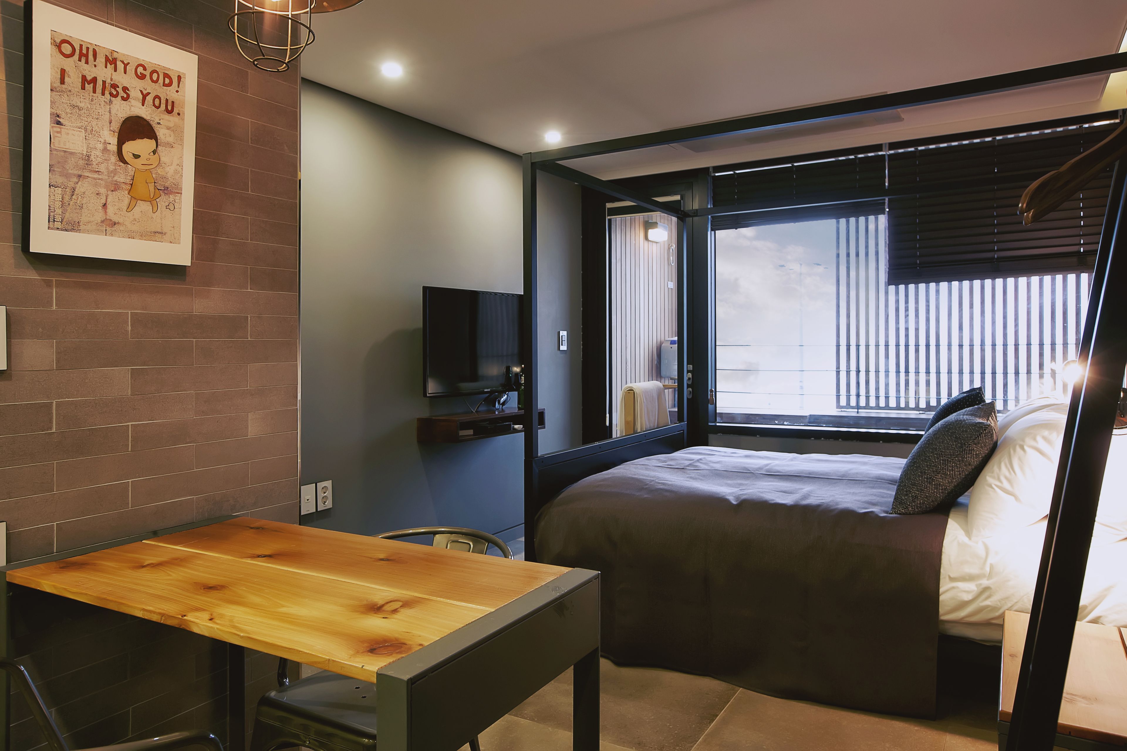 Ein modernes Schlafzimmer mit einem großen Bett, einem Holztisch, einem Fernseher und einem Fenster mit Jalousien.