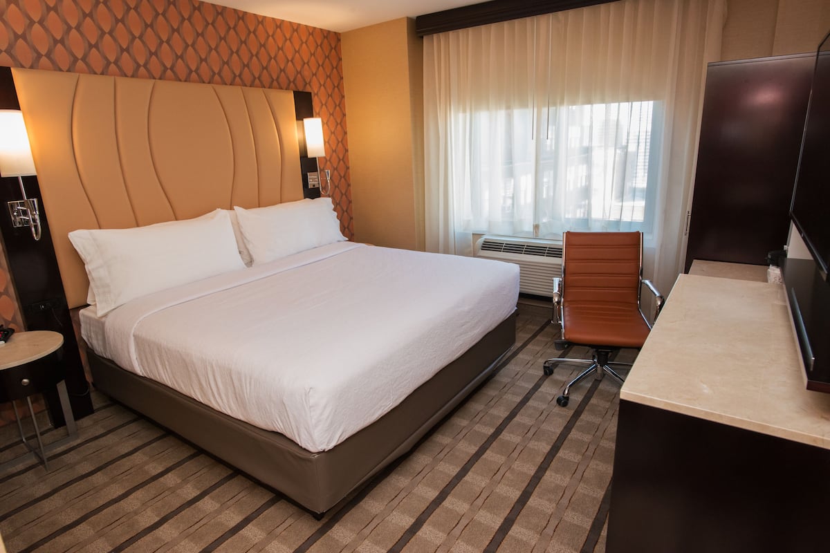 A hotel room with a large bed, a desk, a chair, a TV, and a window with curtains.