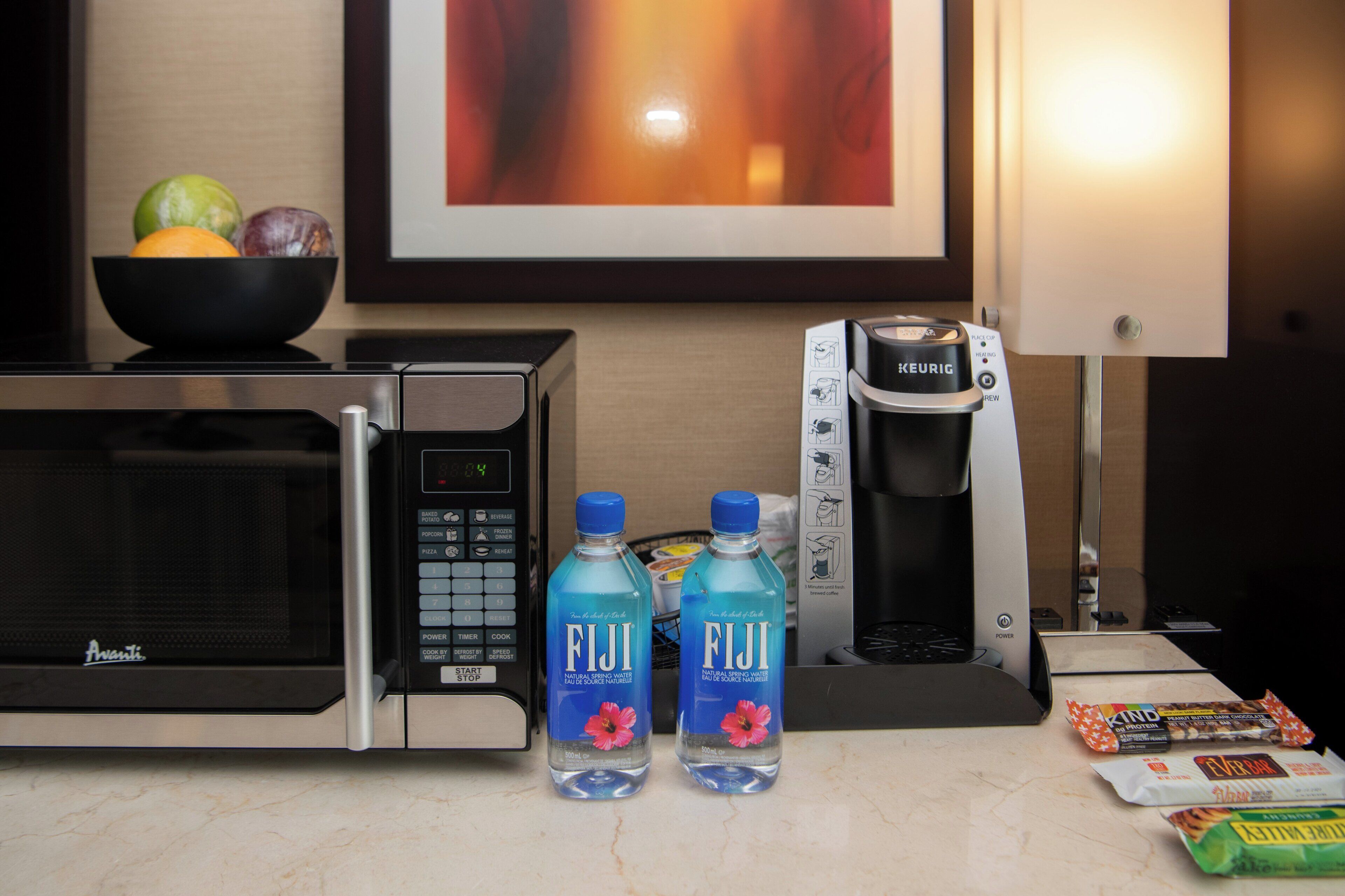 A kitchen counter with a microwave, a coffee maker, and two bottles of Fiji water.