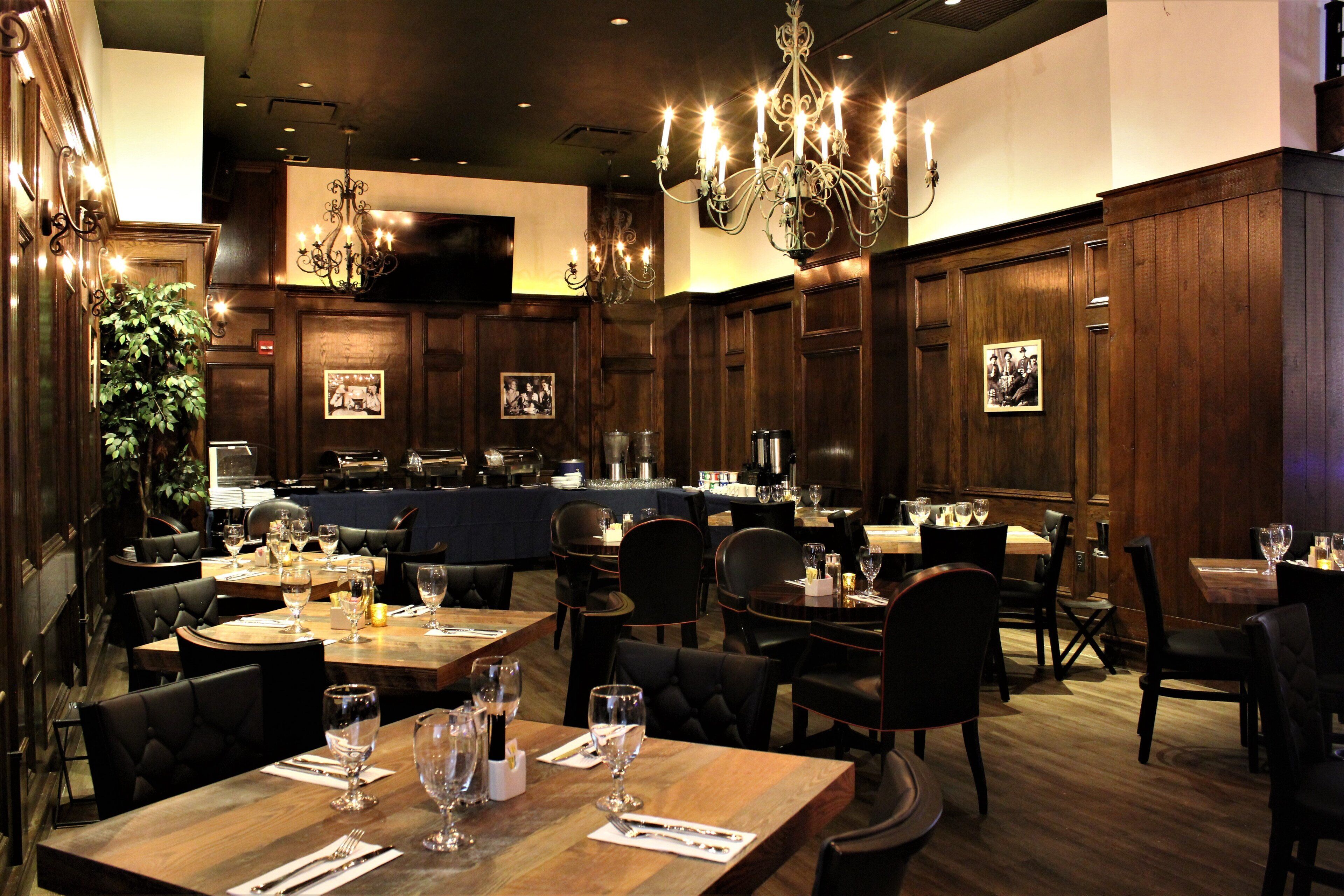 A restaurant with wooden paneling, chandeliers, and tables set for dining.