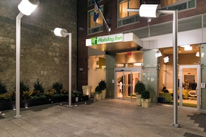 Entrada de um hotel Holiday Inn com fachada de tijolos, portas de vidro e um letreiro acima da entrada.