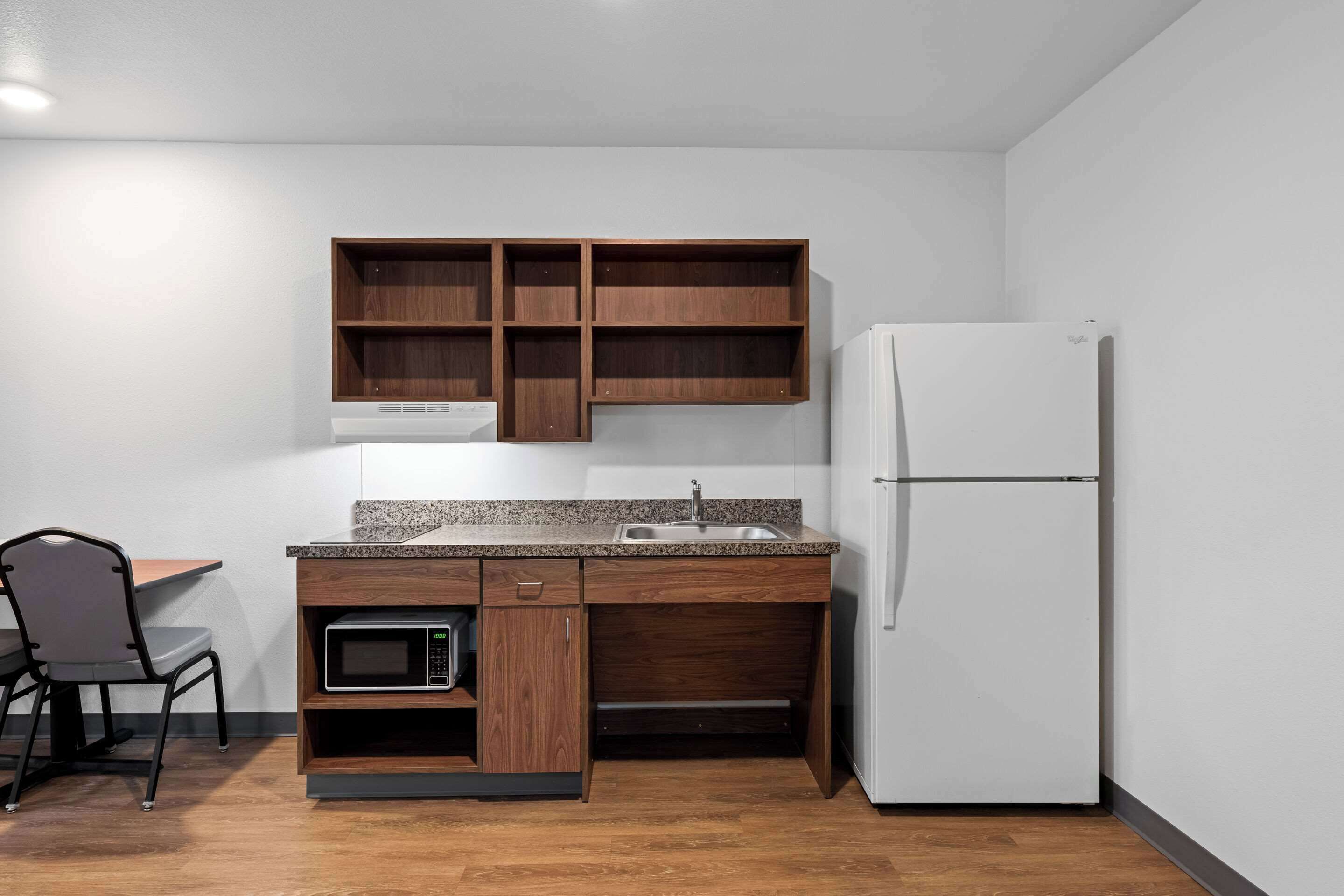 Une cuisine compacte avec des meubles en bois, un four à micro-ondes encastré et un réfrigérateur blanc.