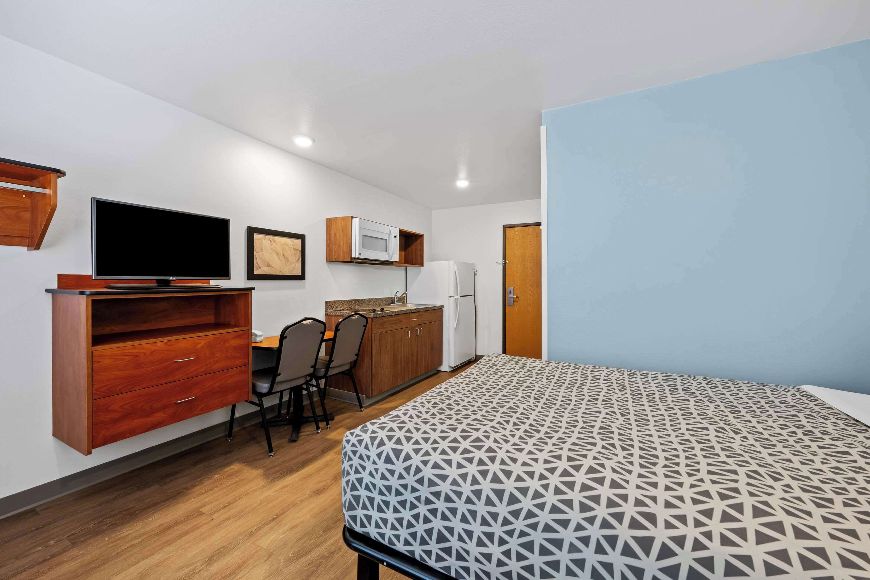 Habitació d'hotel senzilla amb un llit, escriptori amb cadira, televisió, microones i nevera.