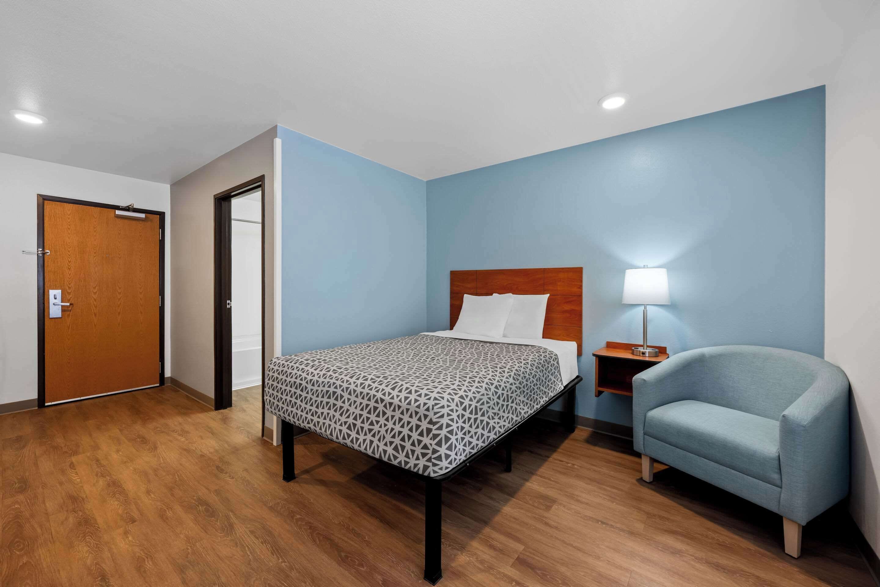 Une chambre d’hôtel avec un lit, une chaise, une table de chevet et une porte.