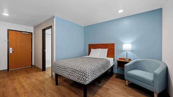 Una habitación de hotel con una cama, una silla, una mesita de noche y una puerta.