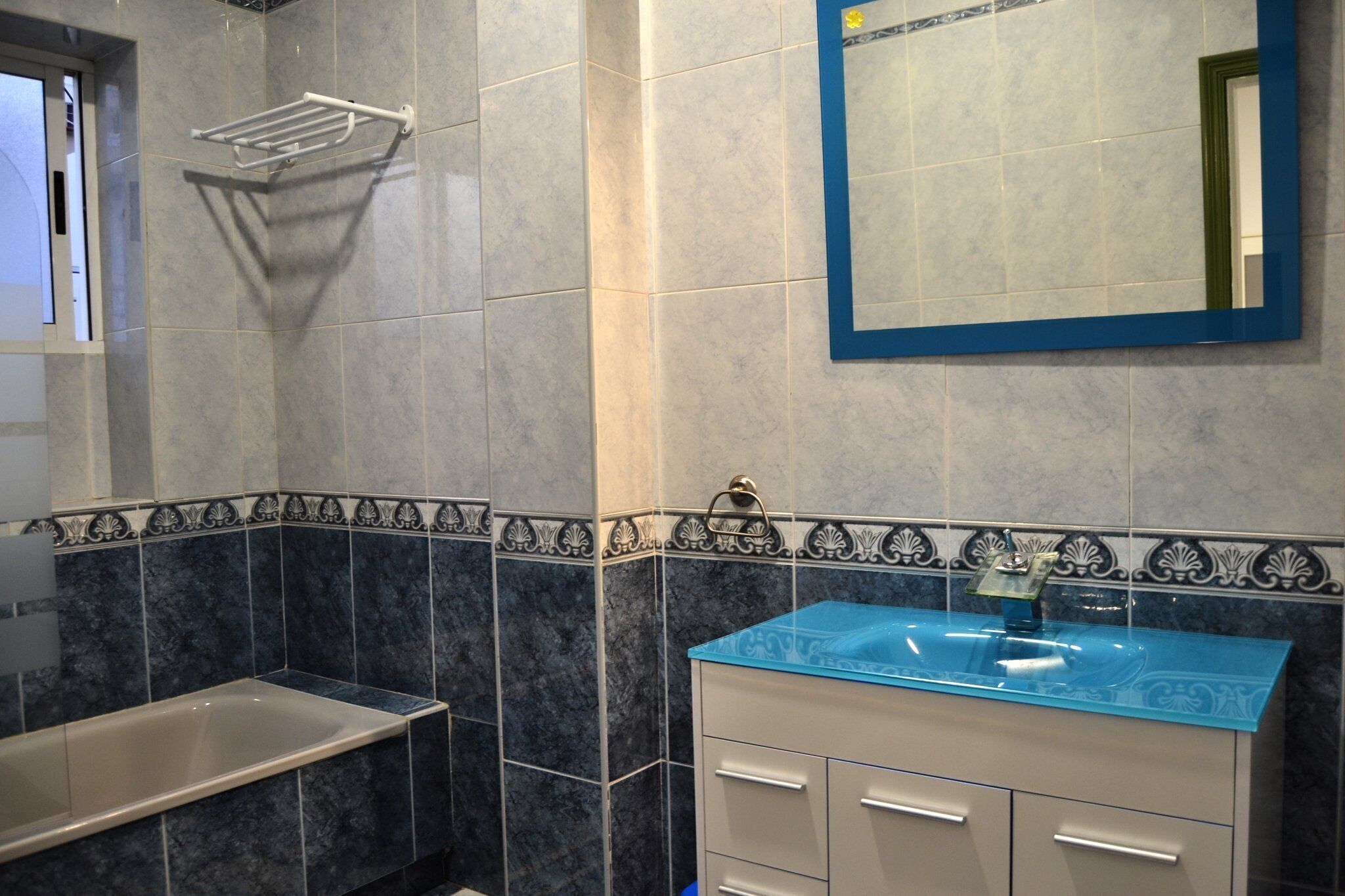 A bathroom with a bathtub, a sink with a blue countertop, and a mirror with a blue frame.