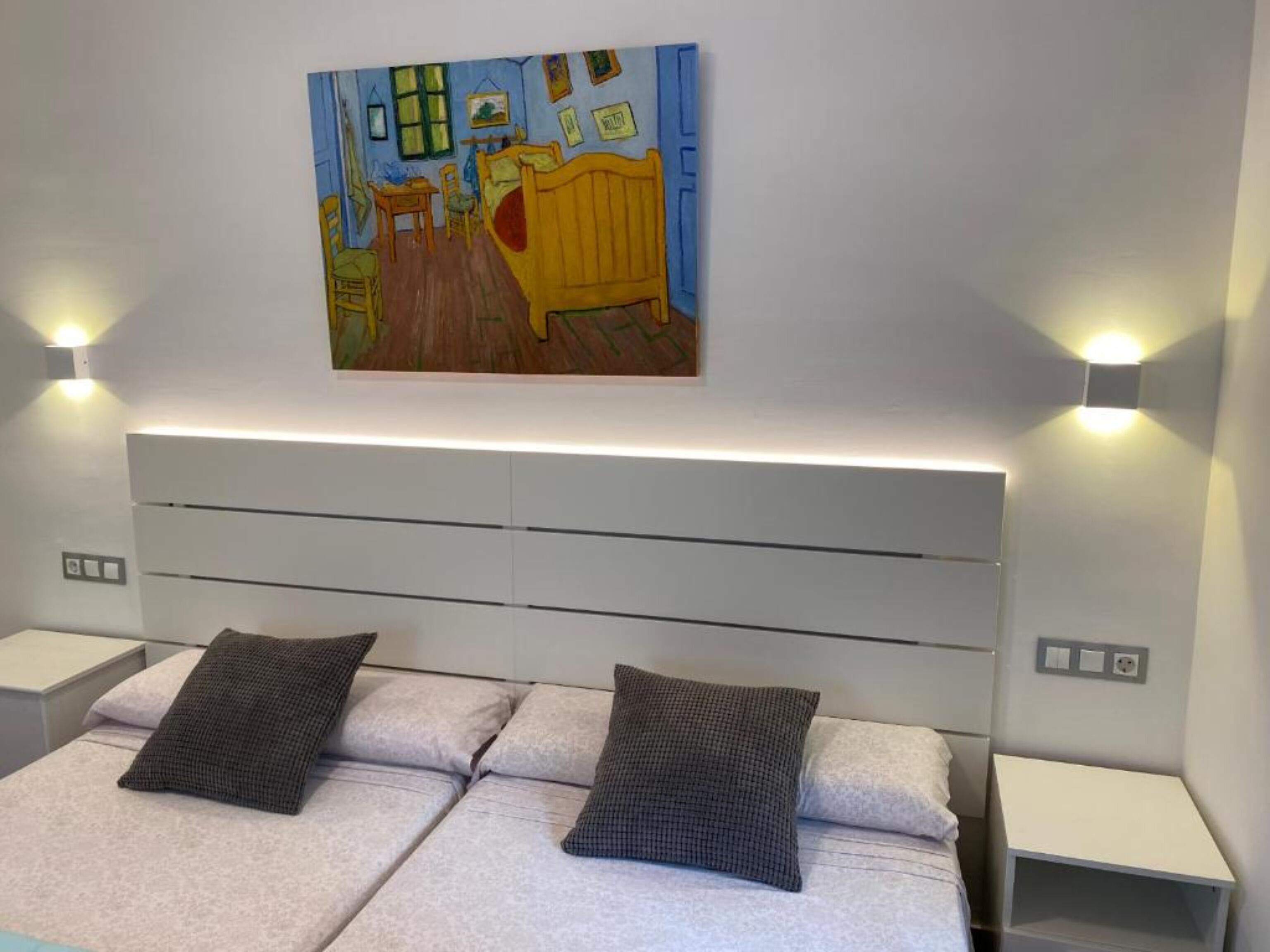 Une chambre d’hôtel comprenant un lit, deux tables de chevet, un tableau accroché au mur et deux lampes murales.