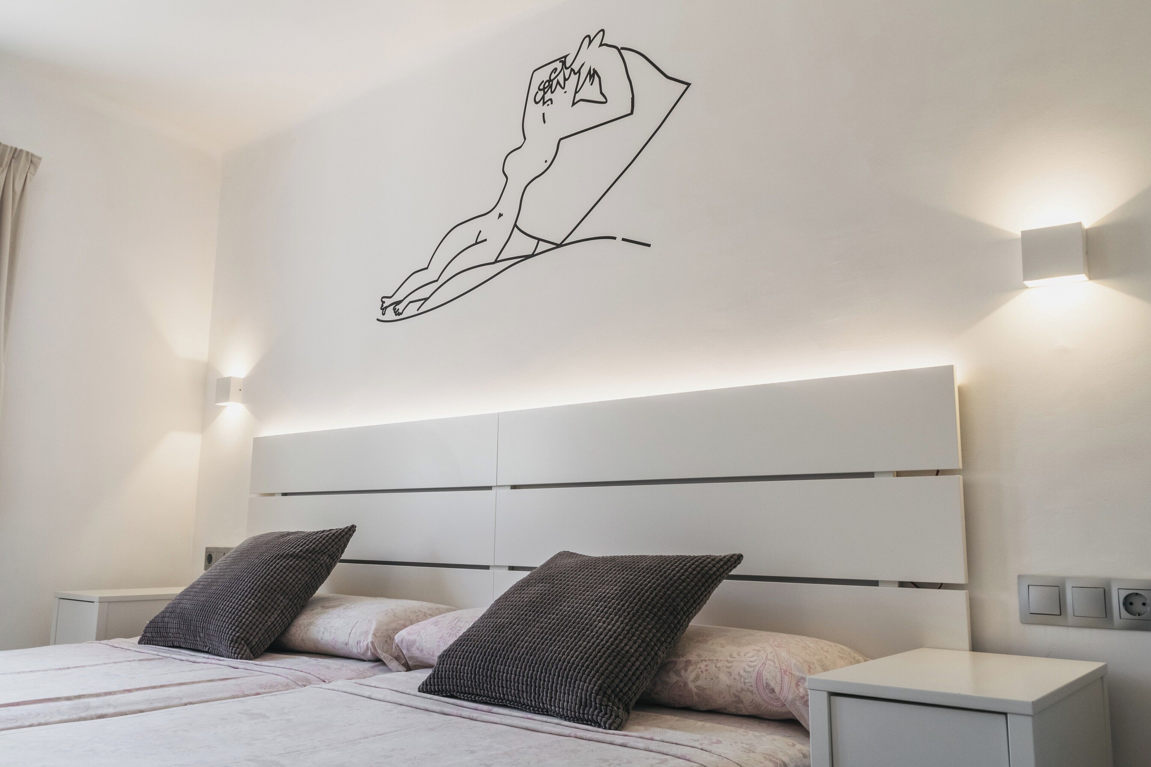 Un dormitorio moderno con diseño minimalista, que incluye una cama con cabecera, dos mesitas de noche y una lámpara fijada a la pared.