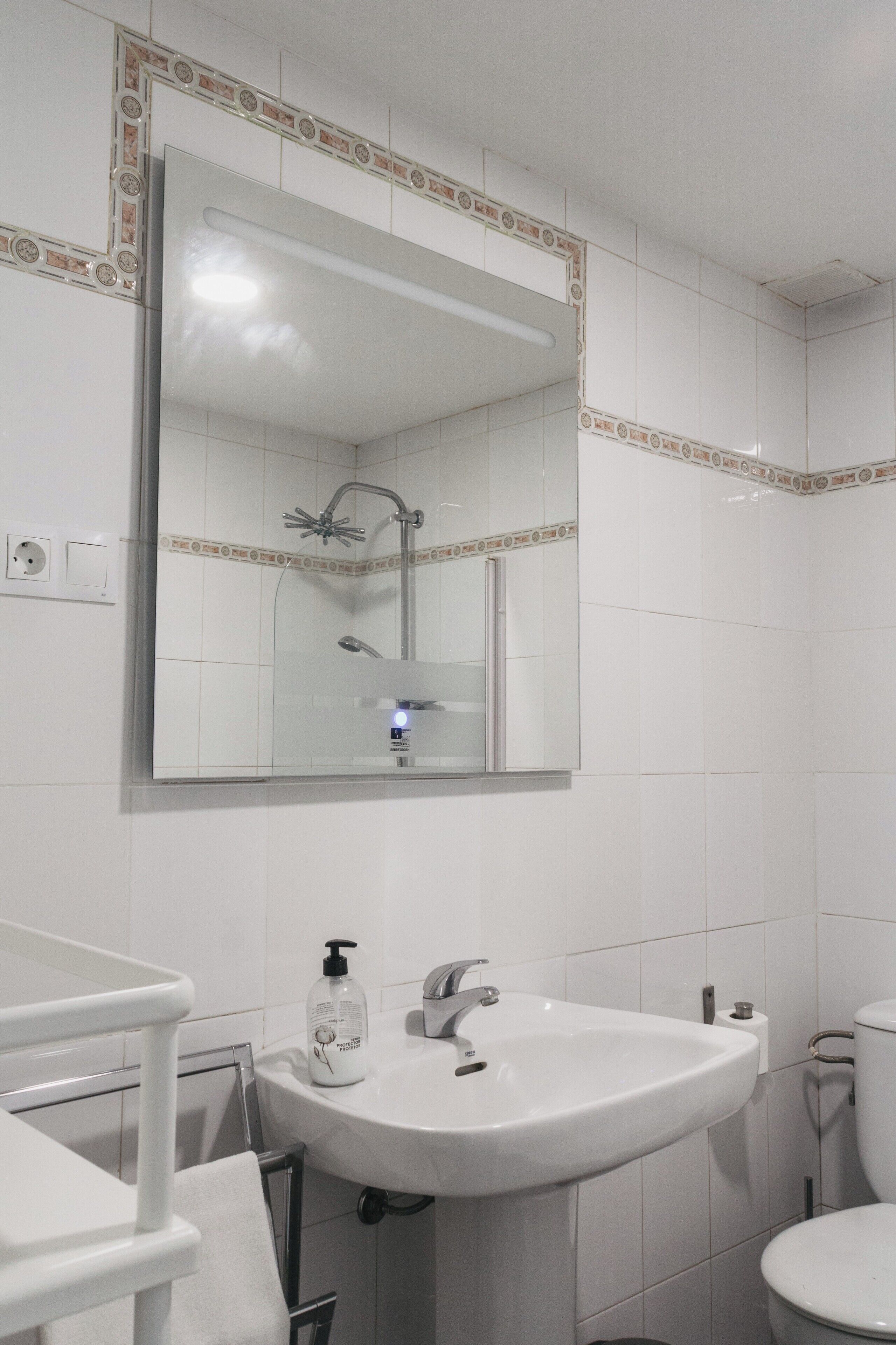 Ein Badezimmer mit einem weißen Waschbecken, einem Spiegel und einer Dusche.