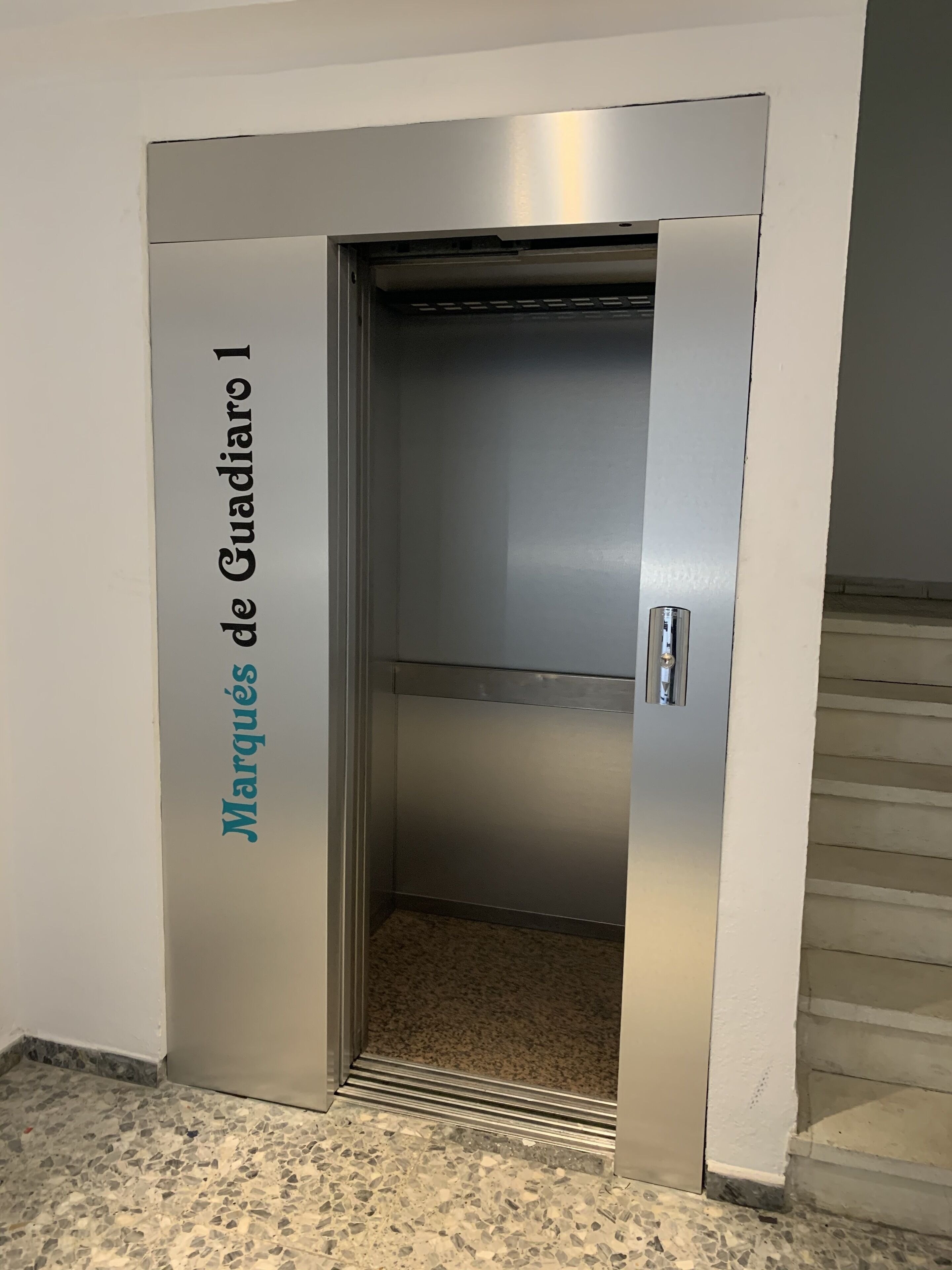 Un ascensor amb acabat metàl·lic i el nom "Marques de Guadiano 1" a la porta.