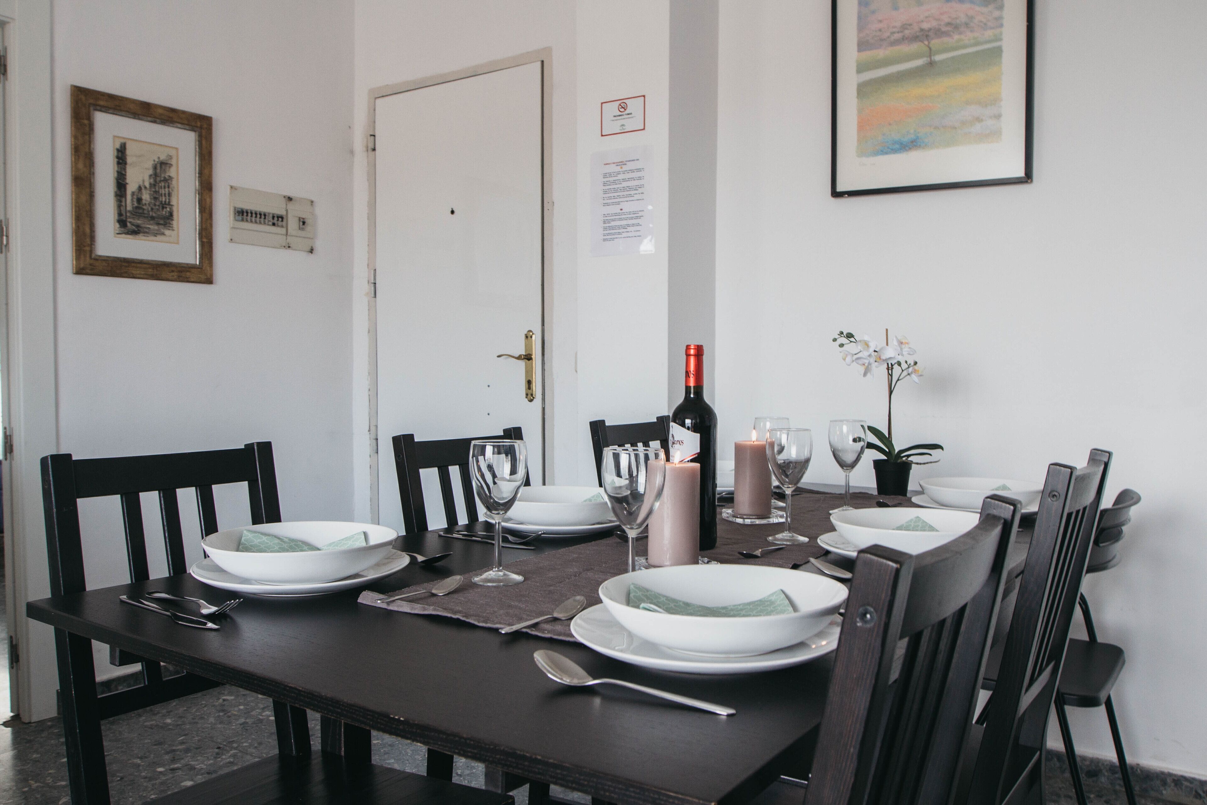 A dining table set with plates, glasses, and cutlery, a candle, and a bottle of wine.