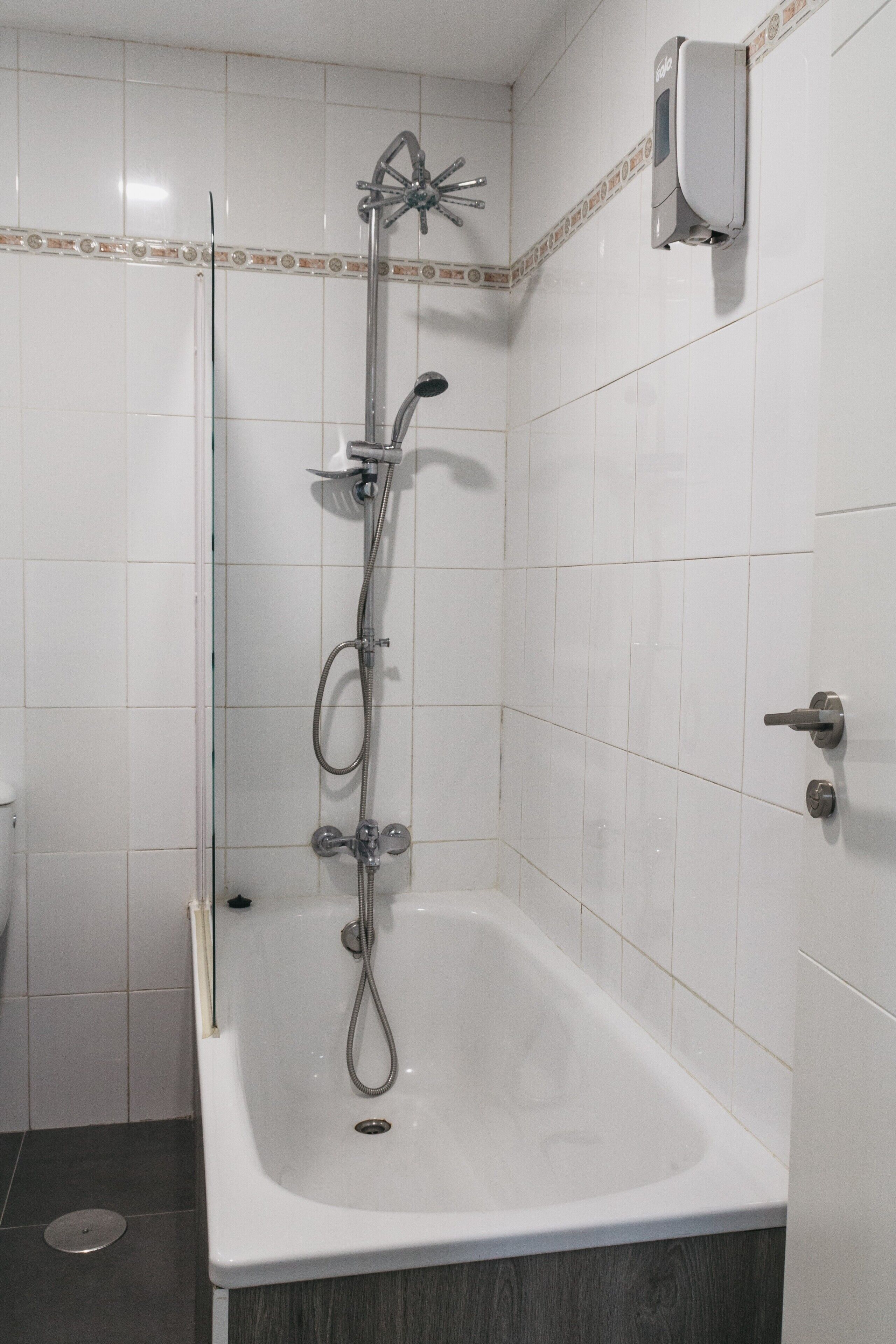 Ein Badezimmer mit einer weißen Badewanne, einer Dusche inklusive Duschbrause und einem wandmontierten Seifenspender.