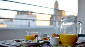 A breakfast setting with a jug of orange juice, a plate with croissants, a glass of orange juice, and a cup on a table with a colorful placemat.