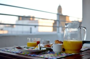 Desayuno con una jarra de jugo de naranja, un plato de cruasanes, un vaso de jugo de naranja y una taza sobre una mesa con un mantel individual colorido.