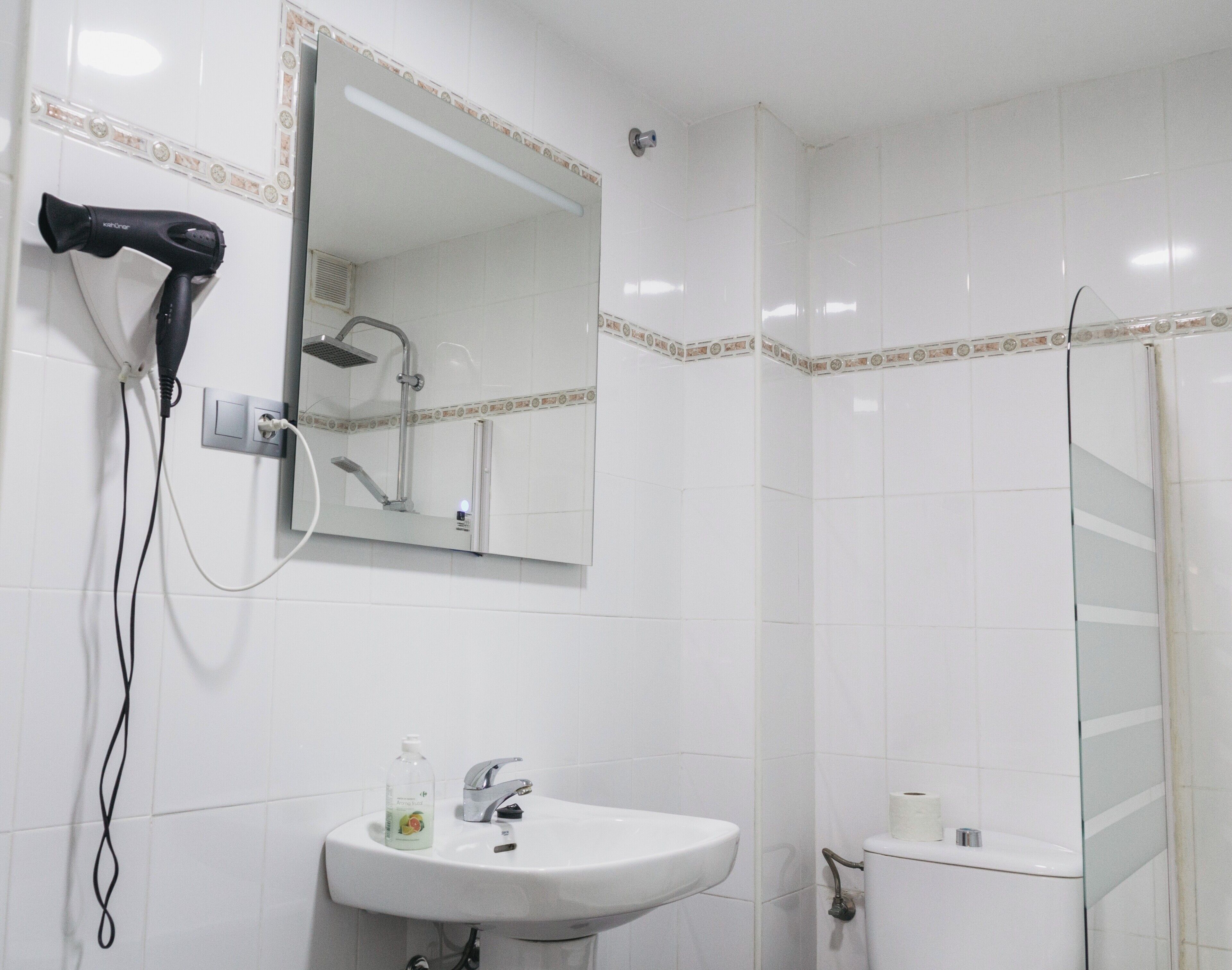 Une salle de bain avec un lavabo blanc, un miroir, un sèche-cheveux et une douche.