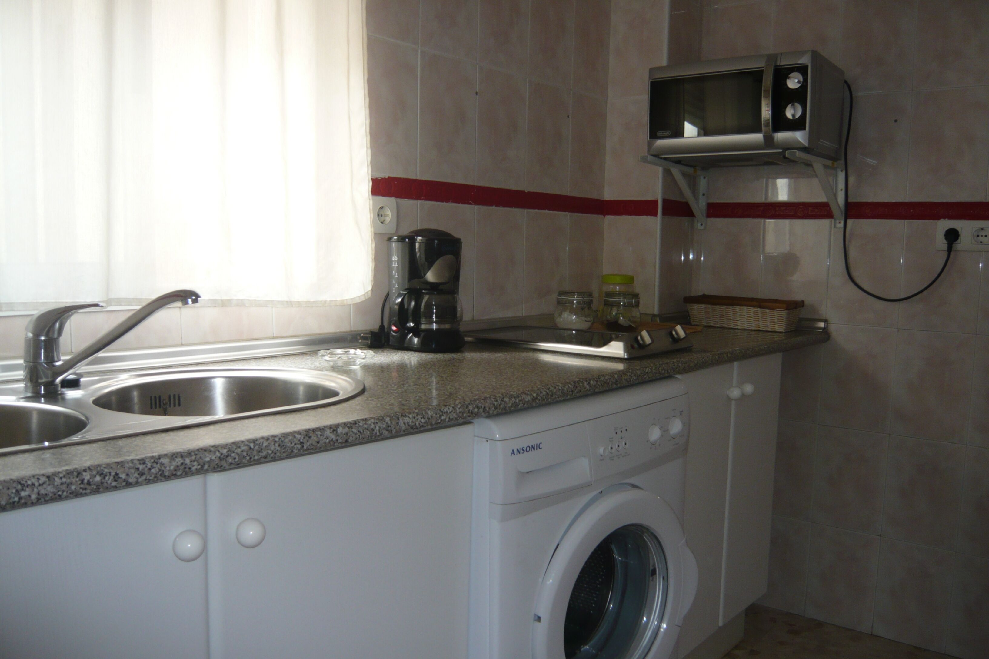 A compact kitchen with a washing machine, a coffee maker, and a microwave.
