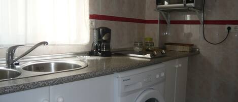 A compact kitchen with a washing machine, a coffee maker, and a microwave.