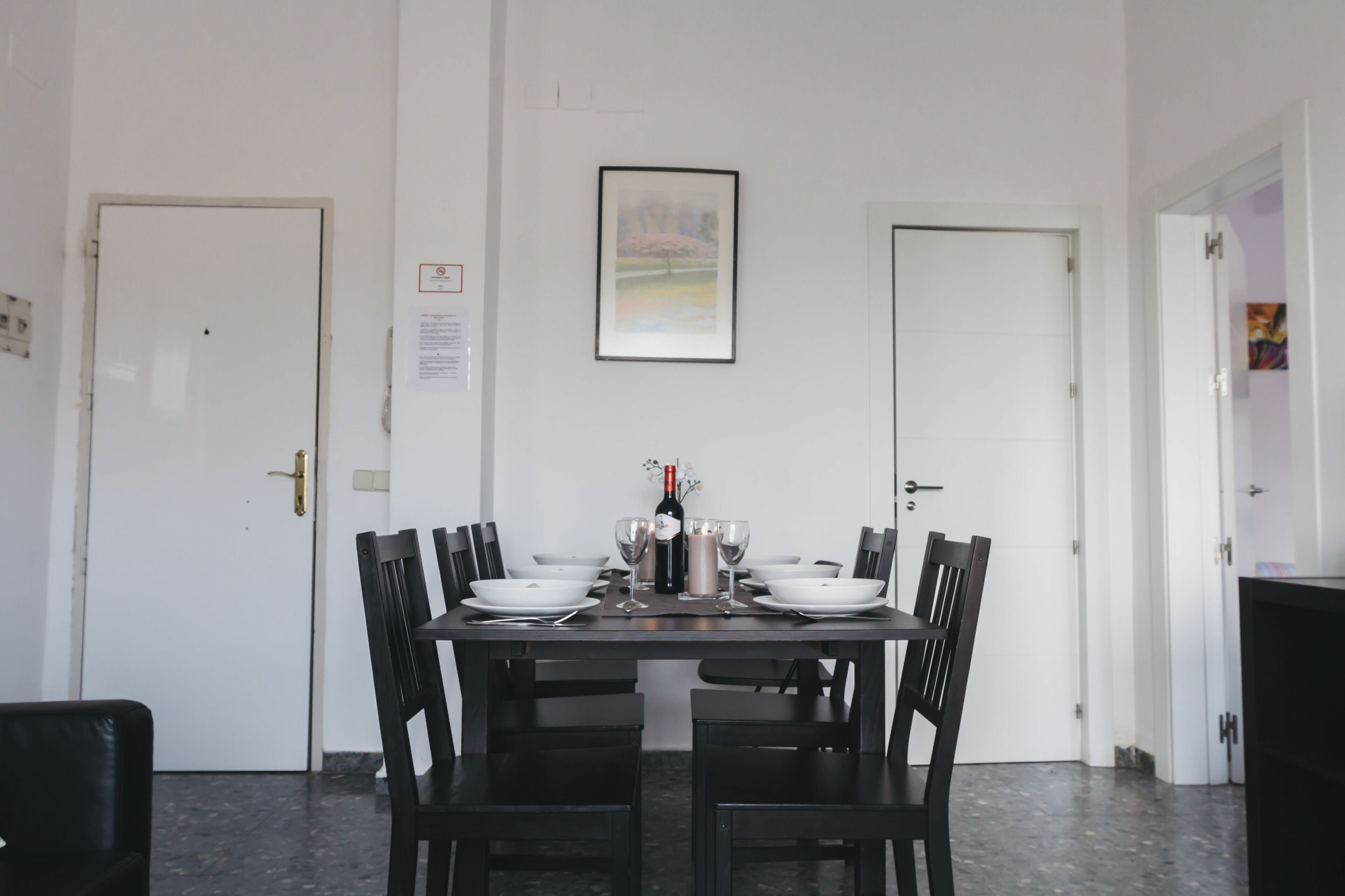 A dining area with a table set for four, chairs, a framed picture on the wall, and a door with a sign.
