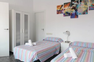 A hotel room with two beds, a wardrobe, a nightstand, and a wall with colorful artwork.