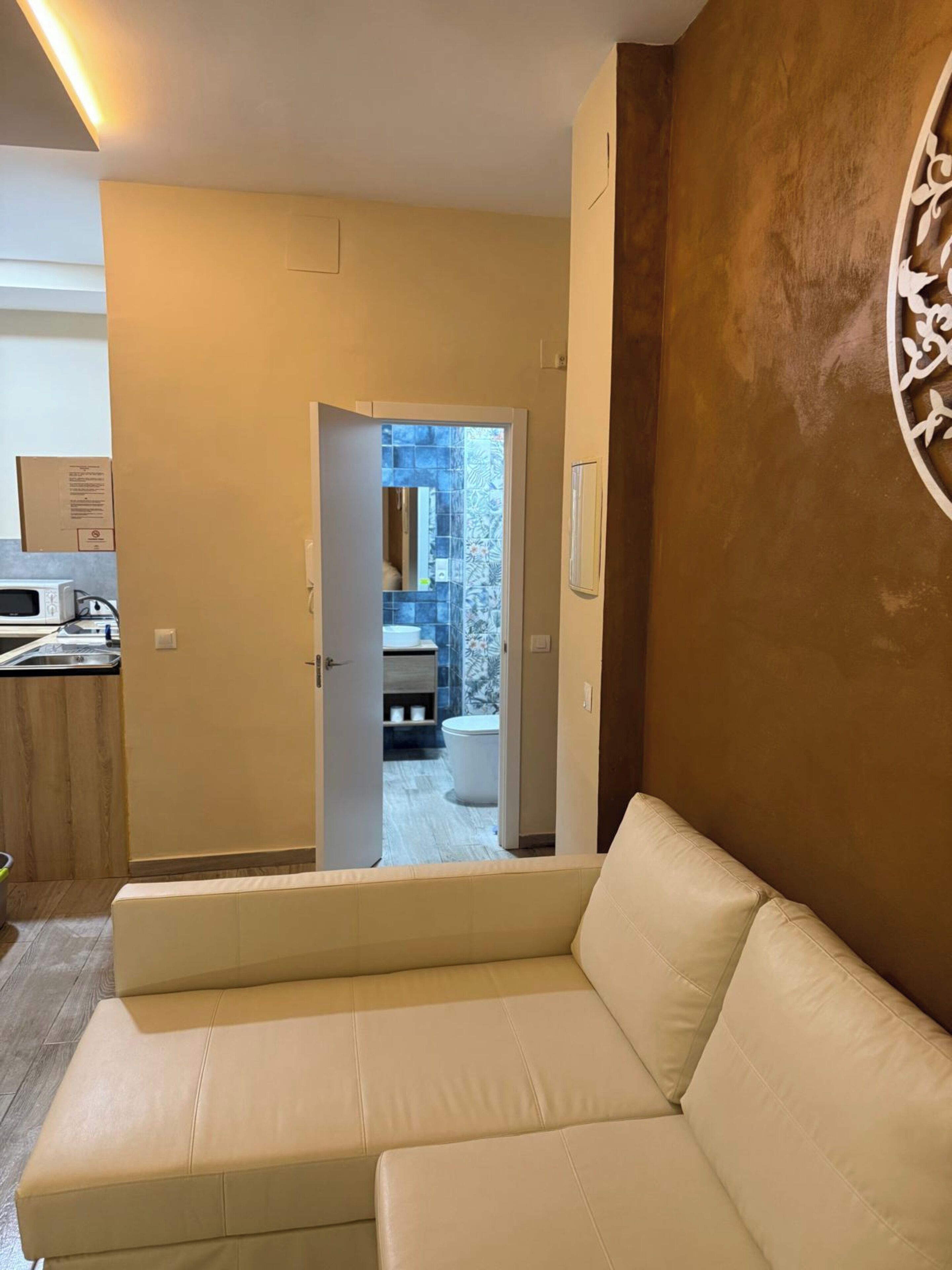 A modern interior with a beige sofa, a wooden accent wall, and a view into a bathroom with a tiled shower.