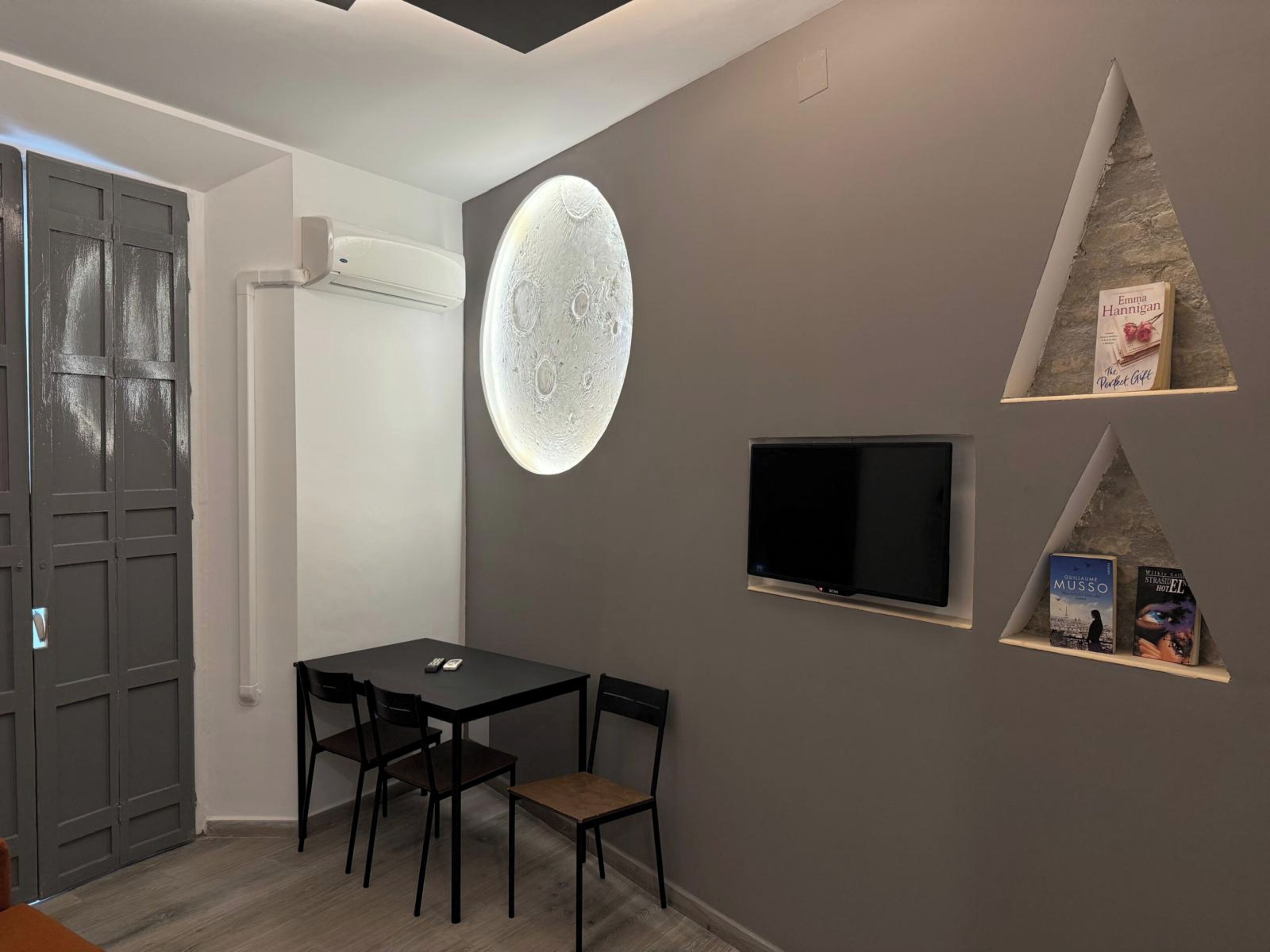 Ein modernes Zimmer mit Esstisch, Stühlen, einem Flachbildfernseher und Bücherregalen mit Büchern.