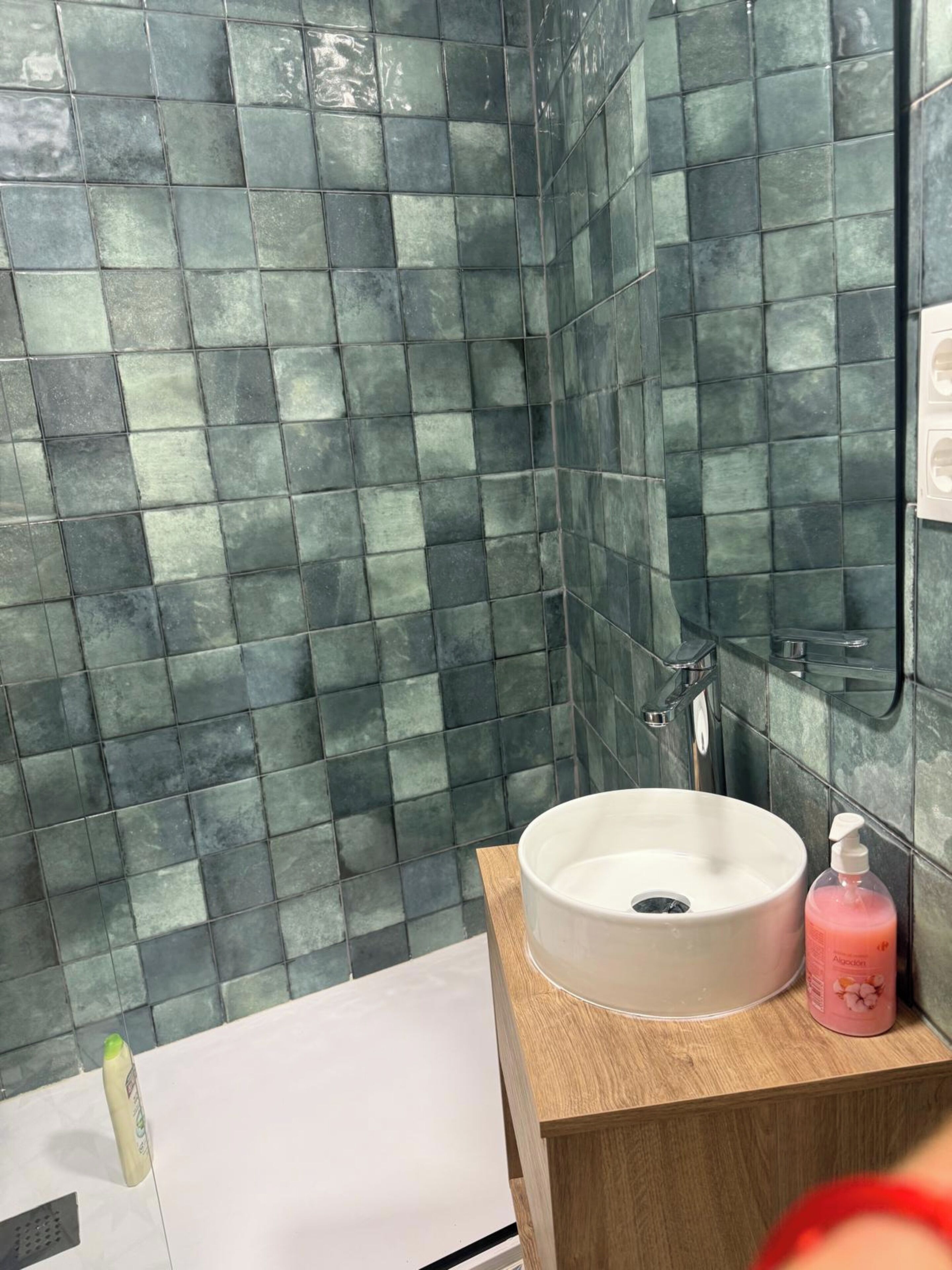 A bathroom with a white sink, a wooden vanity, and a shower area.