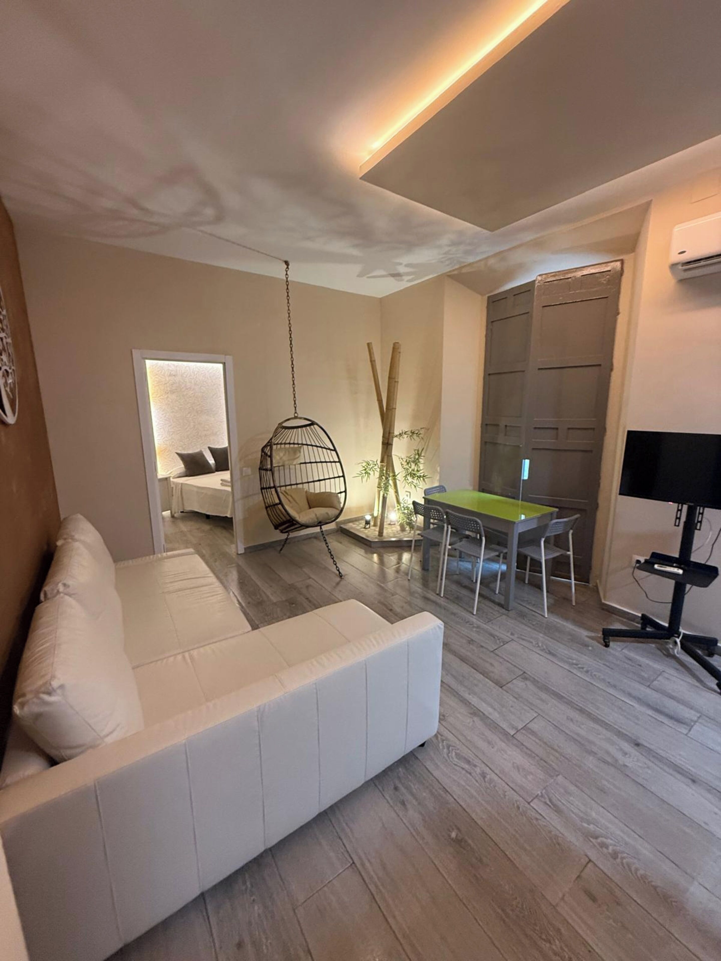 A modern living room with a white sofa, a hanging chair, a dining table with chairs, and a TV stand.