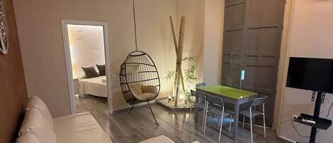 A modern living room with a white sofa, a hanging chair, a dining table with chairs, and a TV stand.
