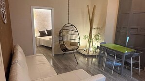Una sala de estar moderna con un sofá blanco, una silla colgante, una mesa de comedor con sillas y un ventanal grande.