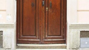 Unas grandes puertas dobles de madera con el número '3' sobre ellas, integradas en un estilo arquitectónico sencillo con una base de piedra y suelo de baldosas.