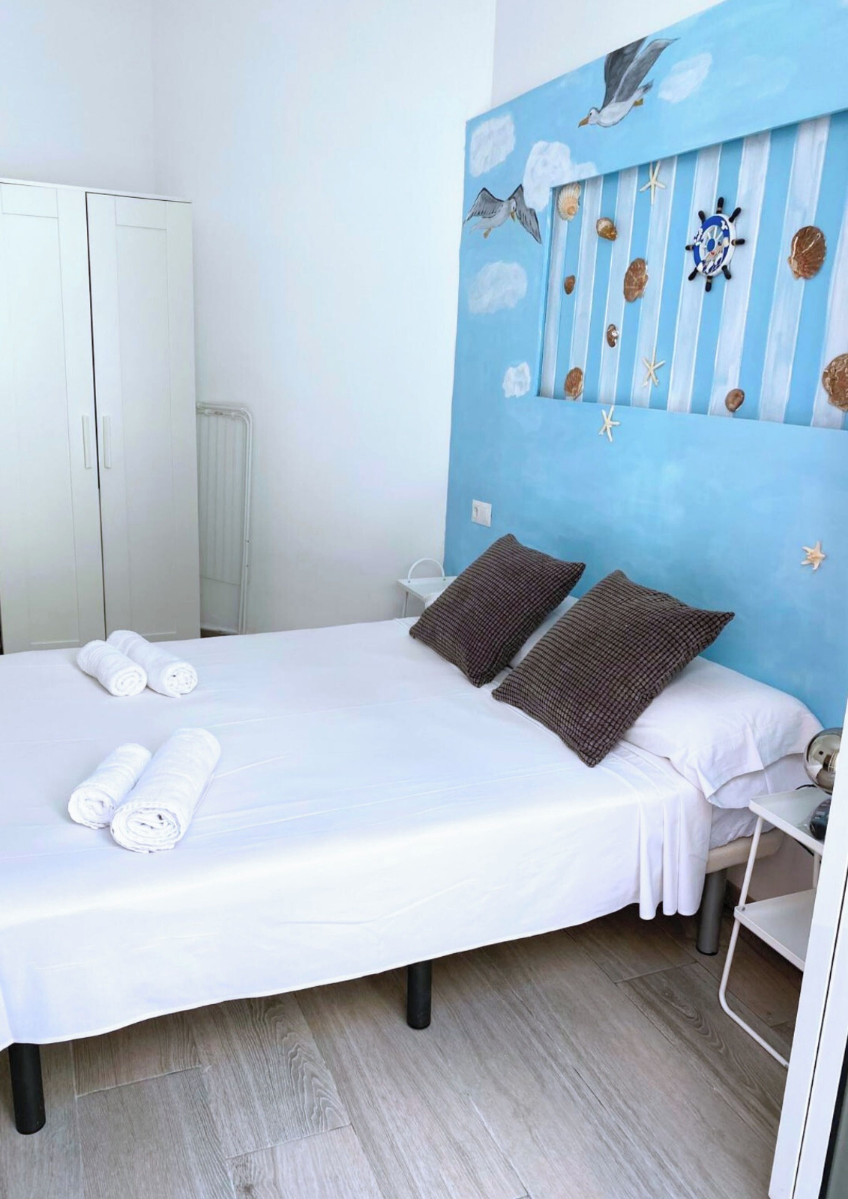 A bedroom with a bed, pillows, towels, a headboard with nautical decorations, and a white wardrobe.