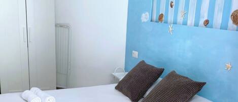 A bedroom with a bed, pillows, towels, a headboard with nautical decorations, and a white wardrobe.